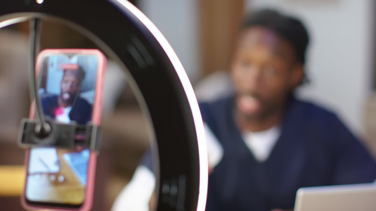 Starting ring-light phone feed African American man showing bottle using laptop explaining at desk