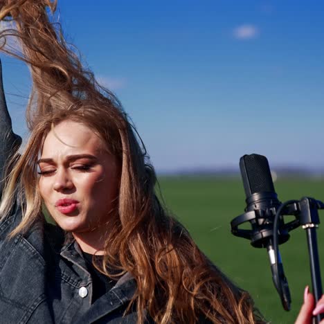 attractive woman performing on green field background. beautiful girl in denim suit singing in a microphone and looking at camera outdoors