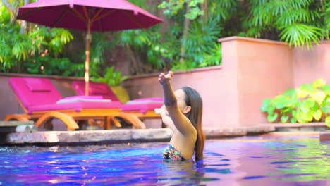 a pretty woman in a very colorful resort pool setting raises her arms to the sky