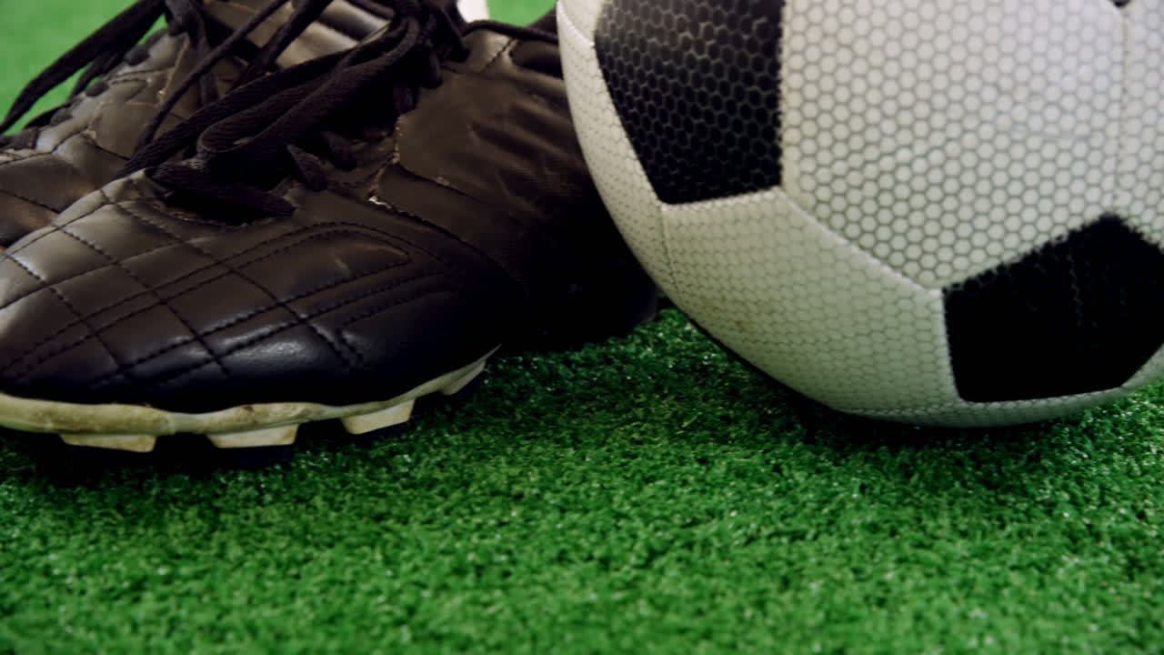 Bola de futebol e chuteiras em gramado artificial 4k