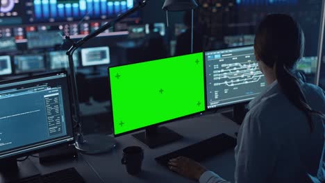 female software engineer working in a modern monitoring office with green screen mock up on a computer display. monitoring room big data scientists and managers sit in front of computers.