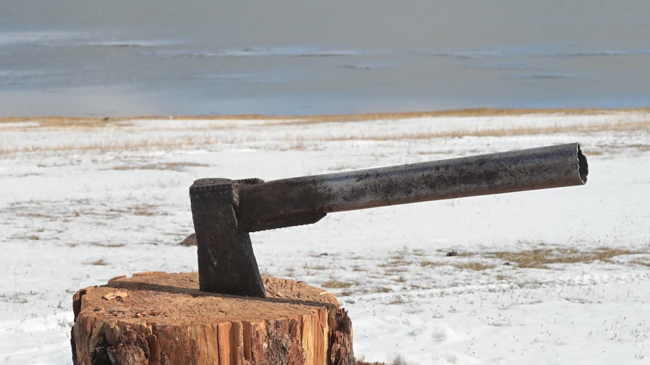 A close-up of an axe in a chopping block contrasts with the vast, snowy landscape of winter in Mongolia. This is a stark and rugged view of a remote, cold environment