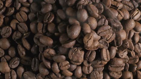 close up top down shot of brown coffee beans on a roasting pan, light smoke being released as the beans are slowly roasted to its familiar coffee characteristics