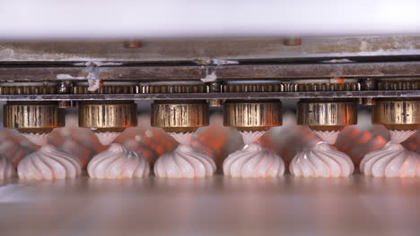 metal rotating nozzles from automatic machine squeezing cream on conveyor. vanilla marshmallow producing at factory. close up.