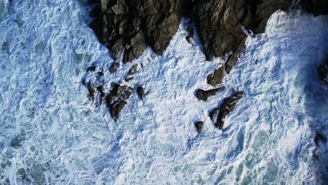 Agua-Blanca-Girando-Alrededor-De-Rocas-De-Pizarra-De-Cornualles-Con-Una-Toma-Aérea-De-Arriba-Hacia-Abajo-En-Cámara-Lenta