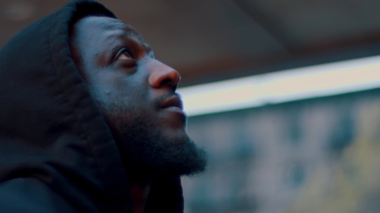 New York, USA, 15 April 2026: American man in black hoodie looking up in city. Profile of man in hoodie looking upwards against blurred urban background with cinematic lighting
