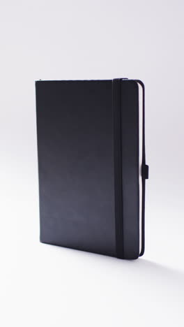 vertical video of closed black notebook vertical with copy space on white background in slow motion