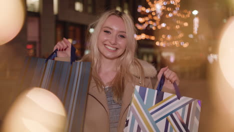 young attractive lady holds up shopping bags and smiles to camera