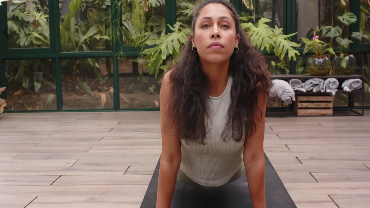 Practicing yoga, woman in glass house doing upward dog pose on yoga mat