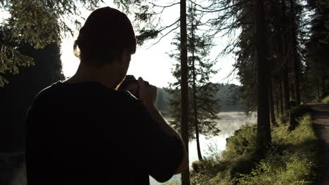 hombre tomando fotos del paisaje del bosque y el lago en una tarde nublada - plano medio