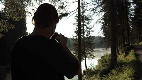 man taking photos of forest and lake landscape in a foggy afternoon - medium shot