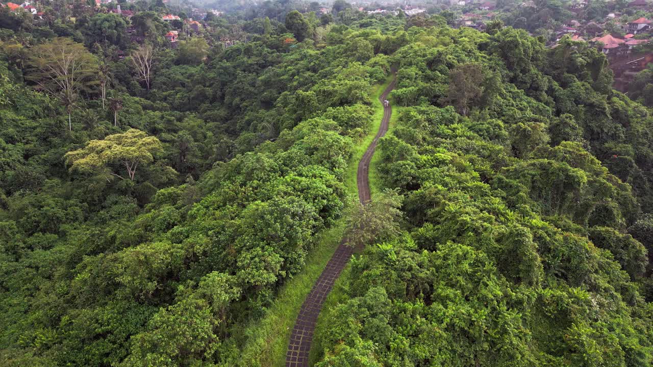 Drone footage capturing a ridge trail across a tropical valley with dense forest and a river below during gloomy weather, showing natural scenery and a peaceful atmosphere across the landscape