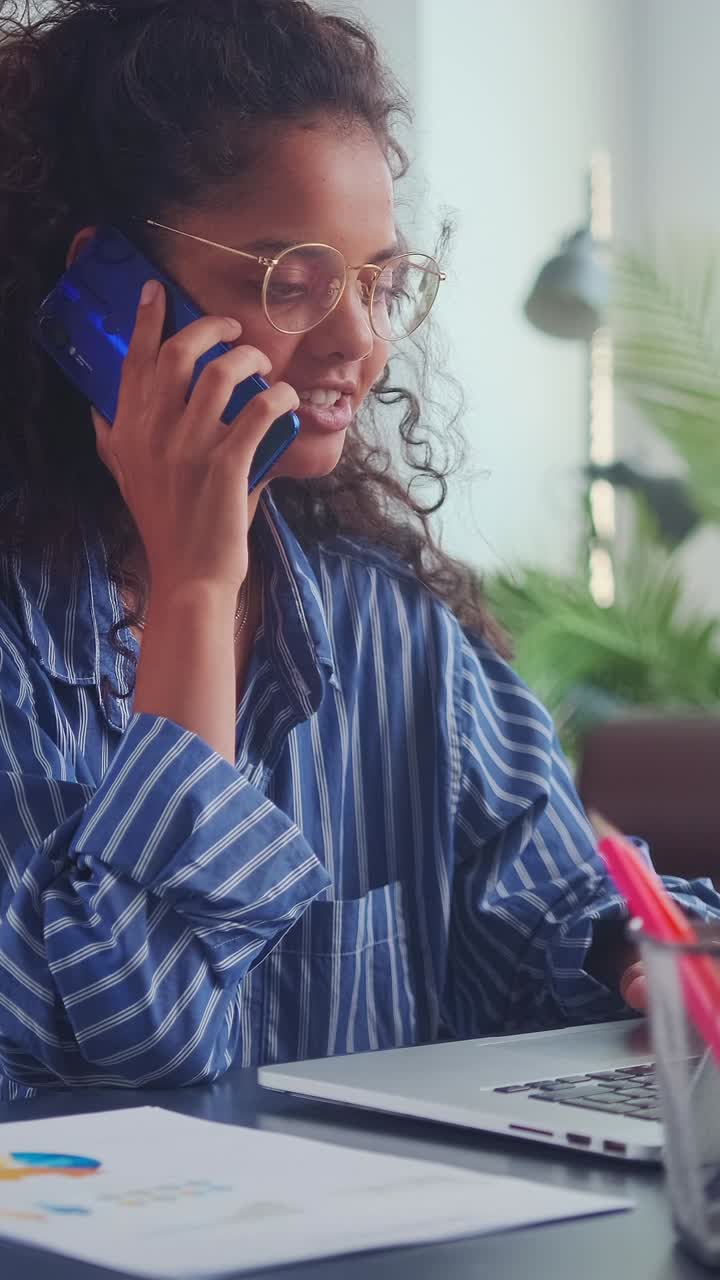 Young woman speaks on phone while working on a laptop at home office