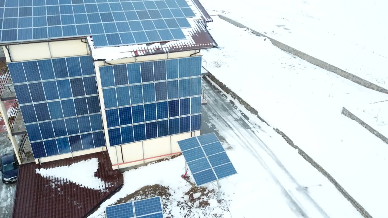 Hotel complex in the mountains with solar panels on the snow. Rows of snow covered solar panels in a small solar power plant.