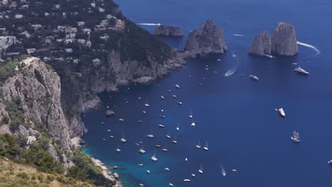 aerial drone shot panning around the faraglioni rocks with luxury boats sailing through the crystal-clear mediterranean sea