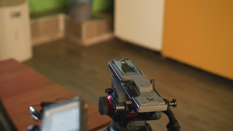 close-up shot of camera tripod head with focus on quick release plate. microphone visible in foreground. background shows home environment with green and orange elements