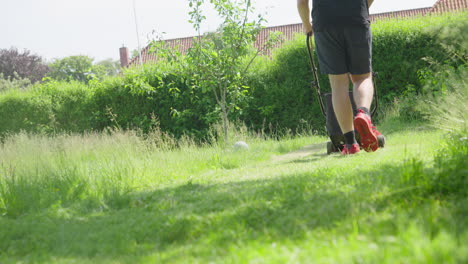 person mowing lush green overgrown lawn with electric lawnmower in sunlight