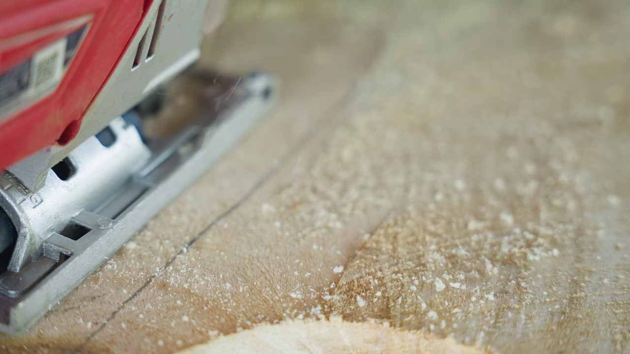 Closeup jigsaw gliding across wood surface, red tool carving gentle arc, sawdust coating plank, steady handheld pass creating even finish, workshop rhythm and focused craft for timber work