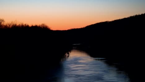 Hermosa-Puesta-De-Sol-En-El-Arroyo,-Bordeada-Por-Un-Cepillo-Sombrío-Al-Atardecer