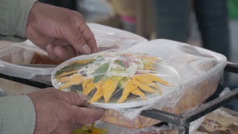 a food vendor wraps a plate of food and prepares to hand it to a customer at a food stall