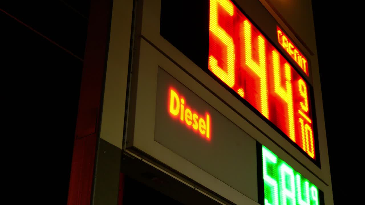 Gas station prices LED light up sign for regular and diesel fuel at night over 5 dollars per gallon credit and cash price, during 2021 2022 war time recession, ground up shot with Dutch angle