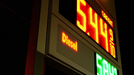 gas station prices led light up sign for regular and diesel fuel at night over 5 dollars per gallon credit and cash price, during 2021 2022 war time recession, ground up shot with dutch angle