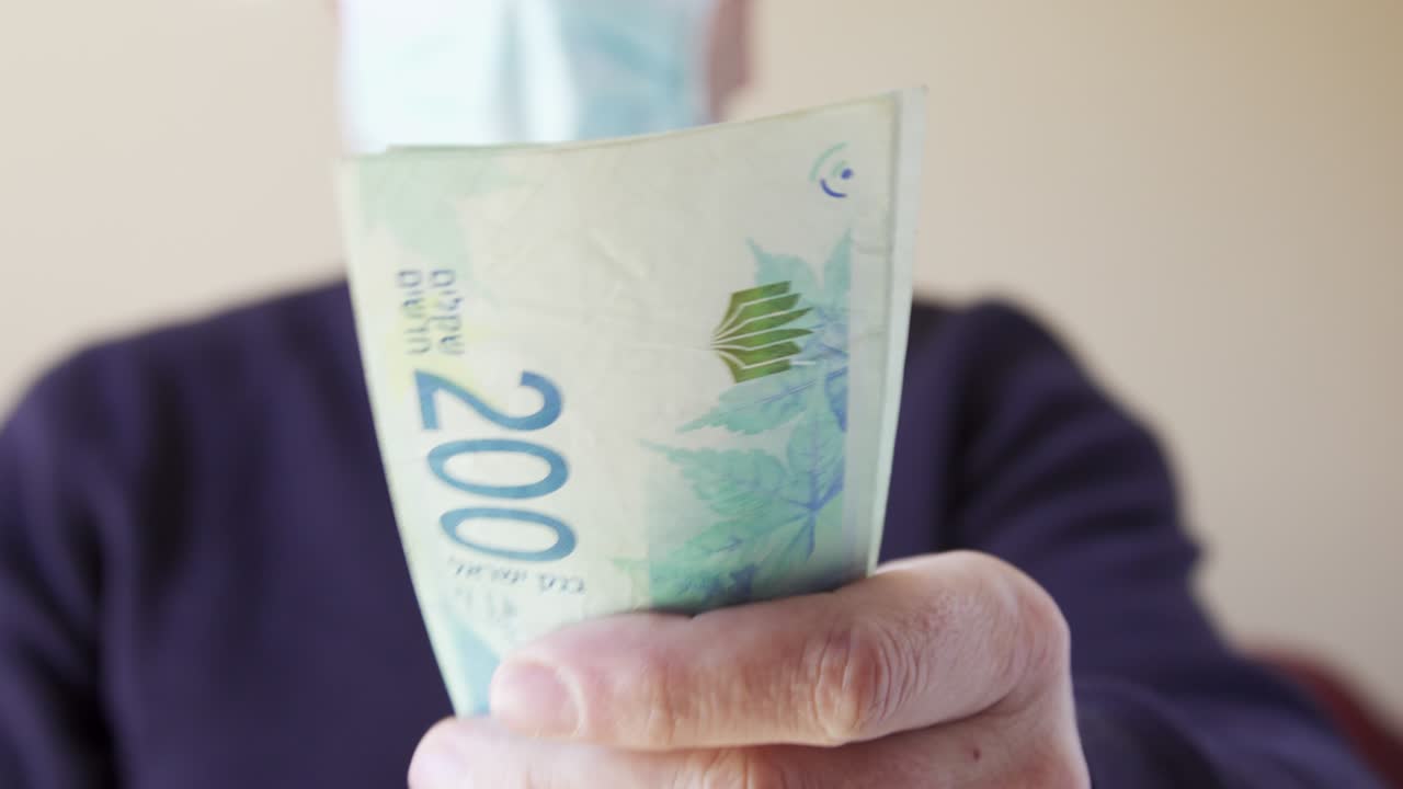 el shekel en efectivo de israel da billetes de papel de moneda. primer plano de un hombre israelí con máscara protectora pagando facturas durante la pandemia