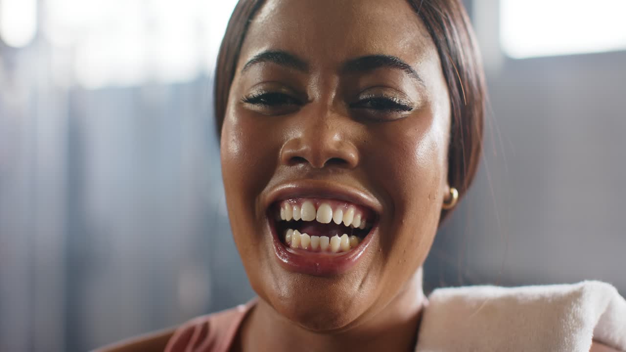 African American woman in gym tank top shifting from smile to laughter holding towel after workout