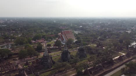 drone captures stunning aerial footage of wat ratchaburana in ayutthaya, thailand, showcasing ancient structures under soft daylight, surrounded by lush greenery and expansive cityscape.