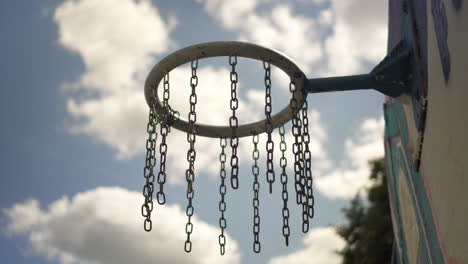 wind moving chains of a basketball ring with blue sky in the foreground