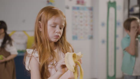 chica pelirroja comiendo un plátano en el aula en una escuela montessori