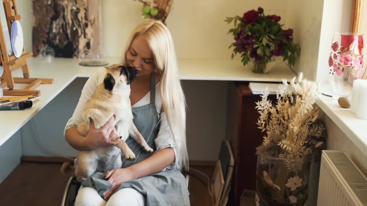 A woman in a wheelchair hugs a pug dog