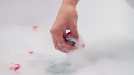 close-up of a hand placing rose petals in a bubble bath