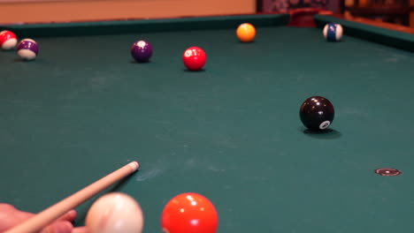 person playing pool shoots green striped 14 ball into far corner pocket using draw or backspin on the cue ball, closeup of bridge hand with wooden cue stick digging into green felt or cloth