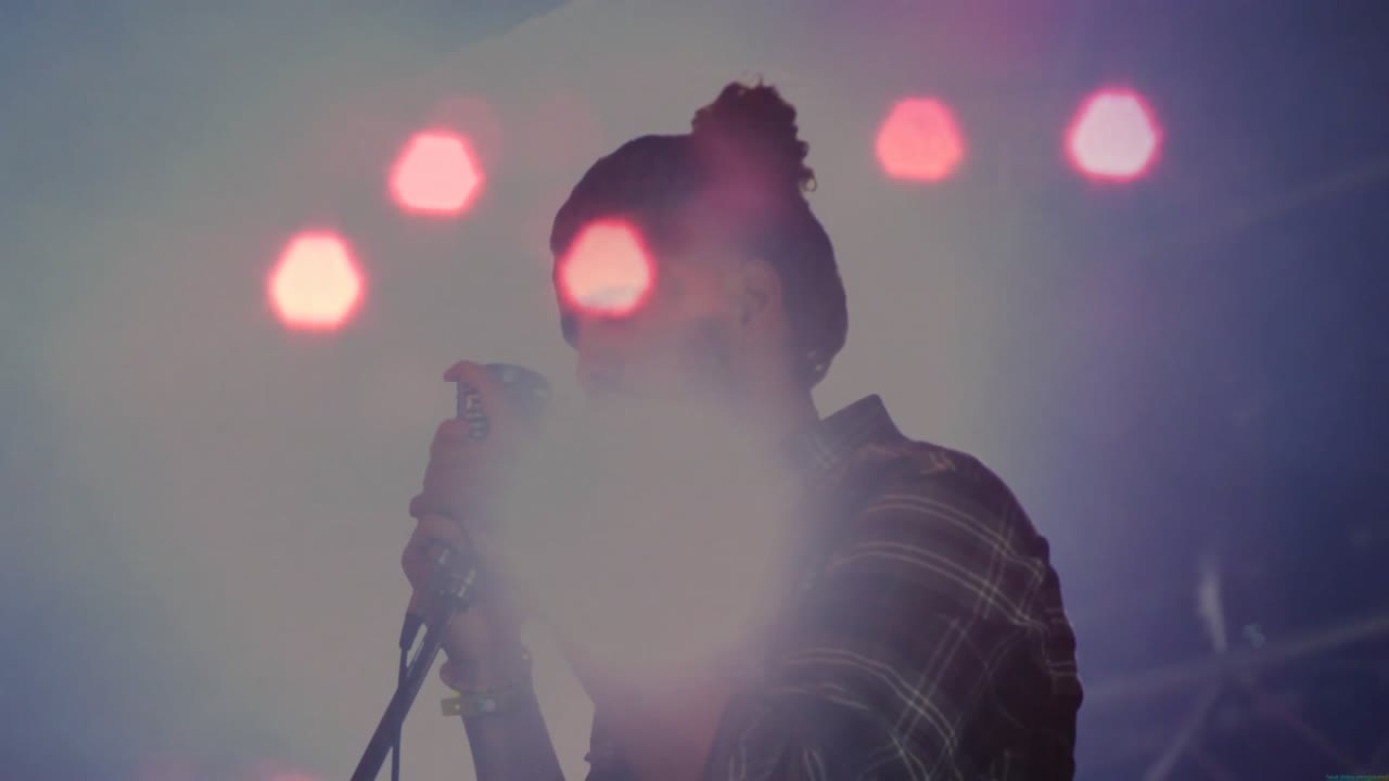 Cantante uomo che impugna un microfono vintage, canta su un palco da concerto con luci soffuse, con bagliori luminosi animati.
