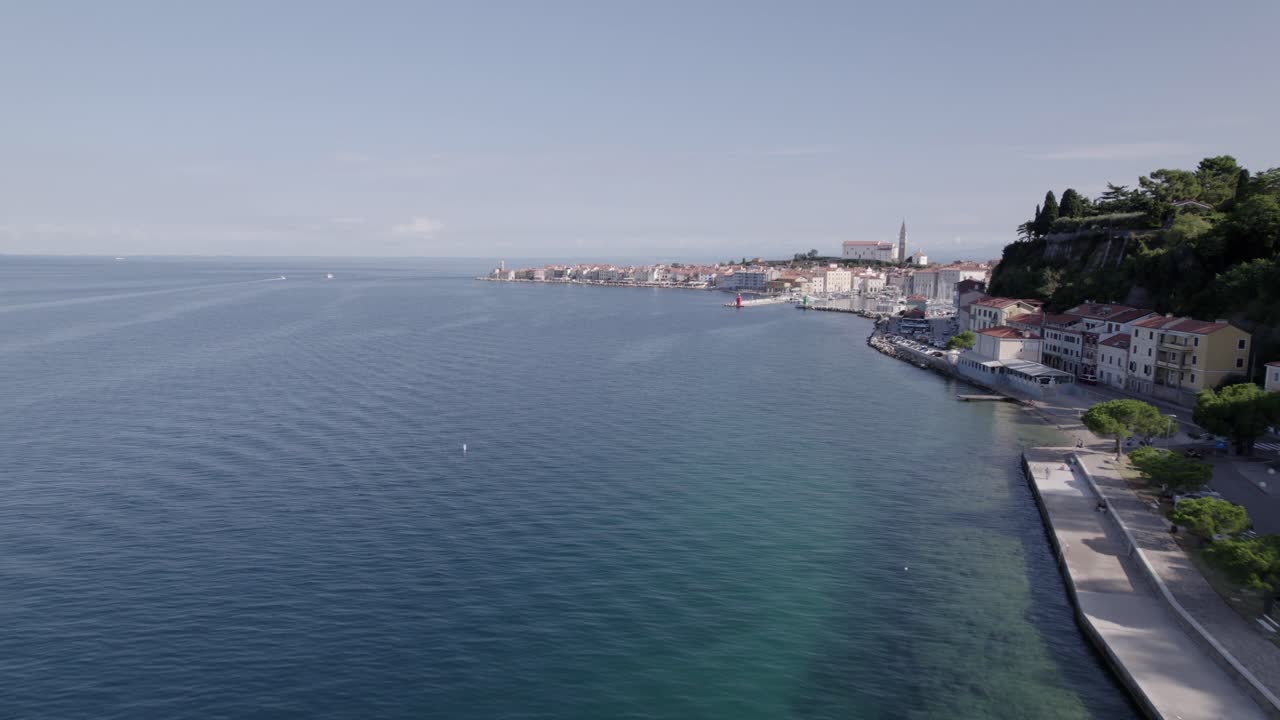 Frontal drone video advancing over the coast of the city of Piran in Slovenia with the seaport and the church in the background, the sky is clear and the flight is a few meters above sea level