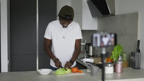 joven hombre afroamericano cortando repollo fresco en la mesa de la cocina mientras cocina ensalada de verduras