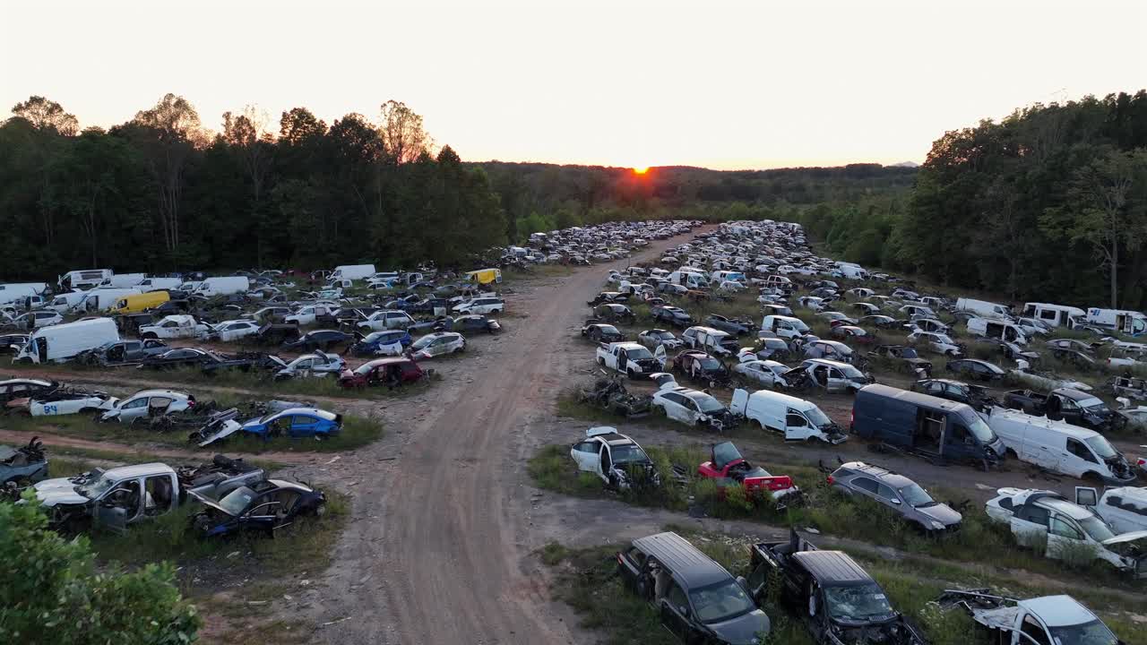 Drone flight over old rusty and destroyed vehicles and trucks on junkyard. American forest landscape at sunset time. Low forward shot
