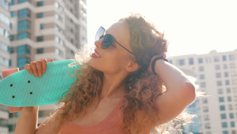 mujer con cabello rizado y gafas de sol sosteniendo una patineta