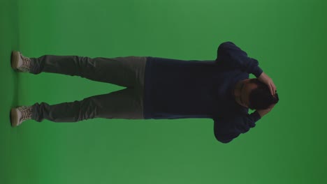full body of depressed asian refugee male rubs his hands through his black hair in despair in the war while standing on the green screen background