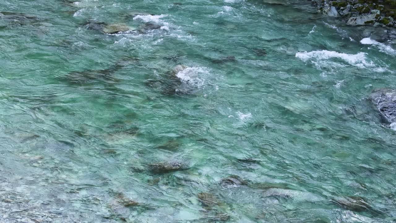 Aerial view of a turquoise mountain stream flowing over smooth rocks, with gentle ripples and natural daylight creating a tranquil outdoor scene