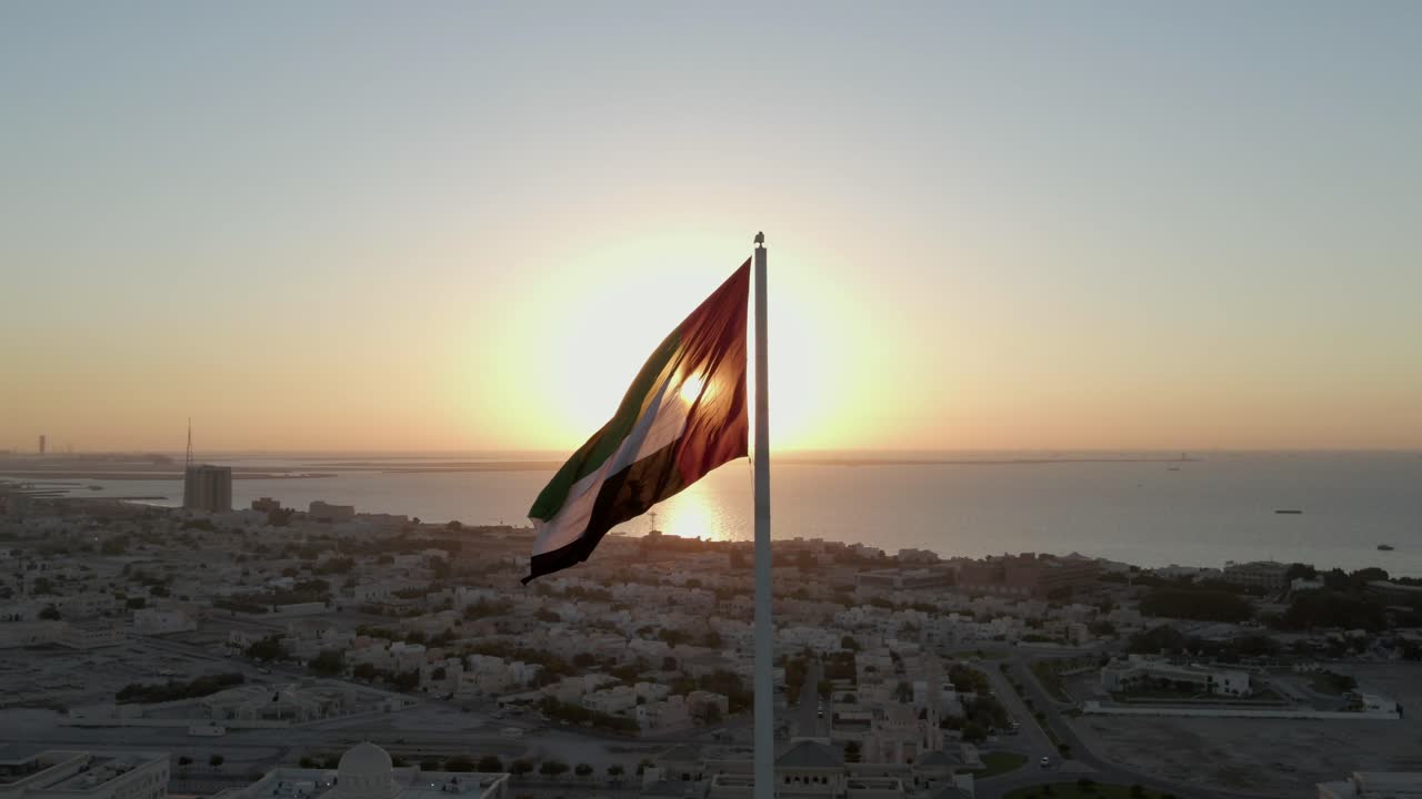 Pemandangan Drone: Siluet, Bendera Uni Emirat Arab berkibar di udara, Latar Belakang Langit dan Matahari, Simbol nasional Uni Emirat Arab
