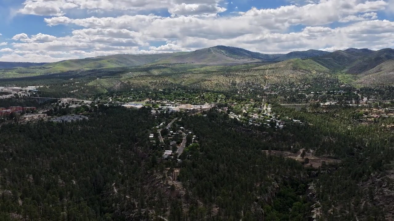 Timelapse 4K panoramico ripreso da drone di una pittoresca città del sud-ovest adagiata su aspre mesas coperte di pini. Ombre drammatiche delle nuvole si muovono attraverso la maestosa valle montana e l'altopiano di fitta foresta.