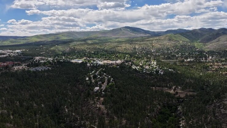 Timelapse 4K panoramico ripreso da drone di una pittoresca città del sud-ovest adagiata su aspre mesas coperte di pini. Ombre drammatiche delle nuvole si muovono attraverso la maestosa valle montana e l'altopiano di fitta foresta.