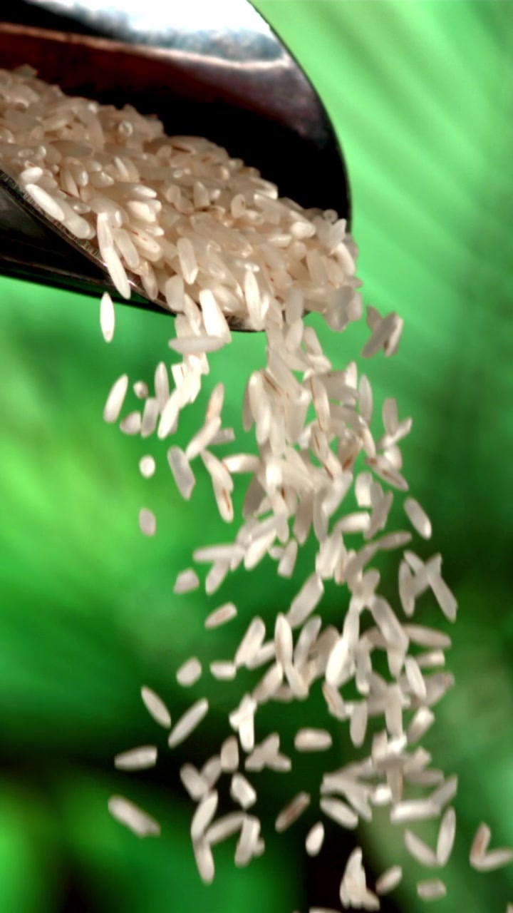 Movimento rallentato di chicchi di riso bianco che si riversano da una paletta di metallo