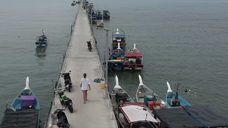 Young-woman-in-white-tee-shirt-walks-along-dock-past-Malaysian-boats