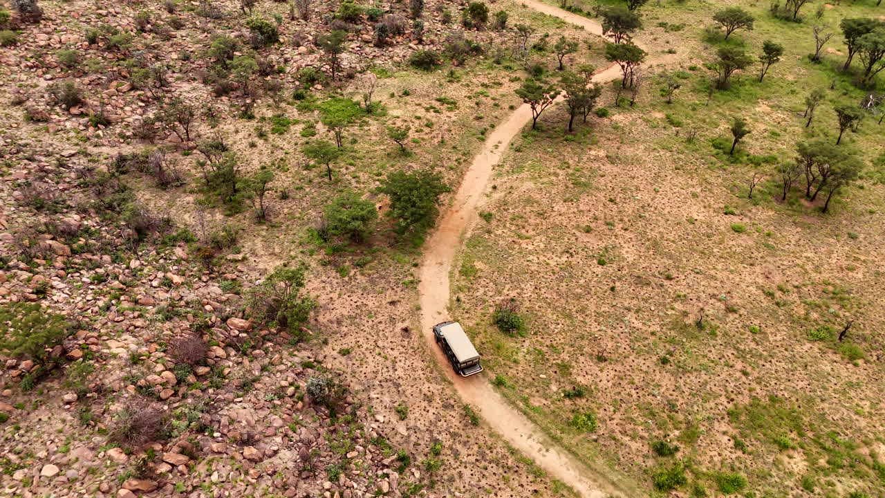Aerial view of safari game drive vehicle on dirt road through African wilderness