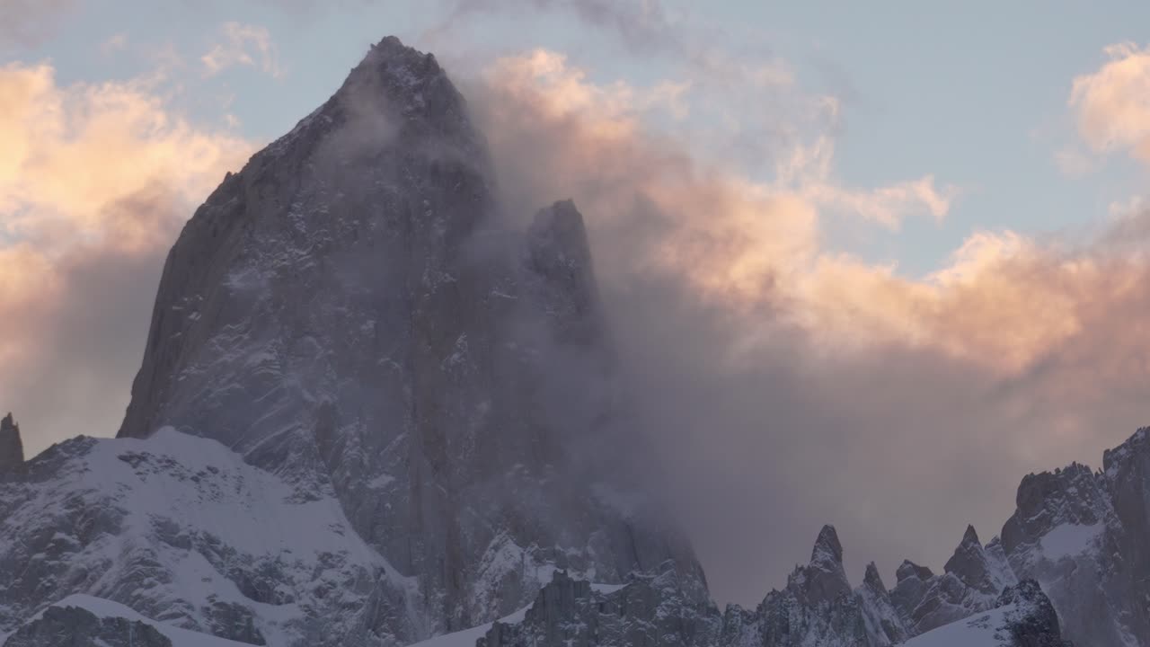 La cima del monte Fitz Roy circondata da nuvole vorticose durante un tramonto vibrante, che mostra la grandezza della natura.