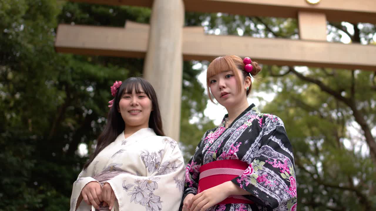 Due donne sorridenti in kimono tradizionali stanno davanti a un grande cancello torii di legno a Tokyo
