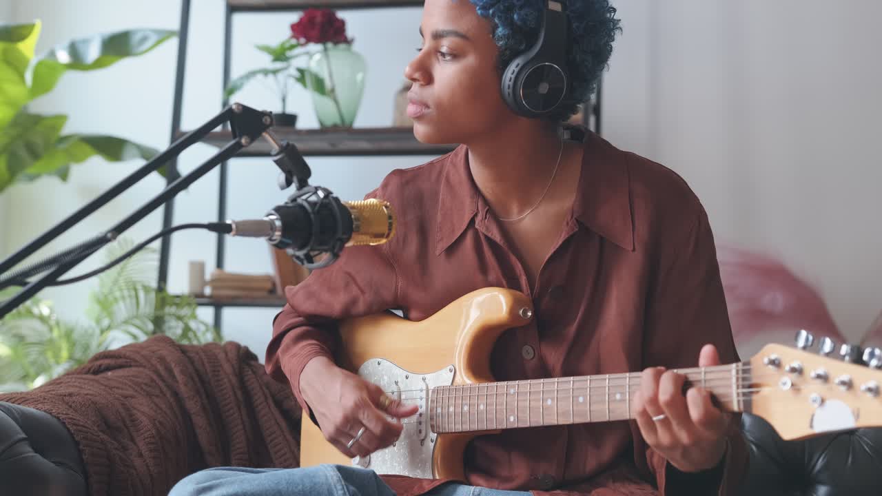 Young african american woman playing cool music on guitar sits in home studio